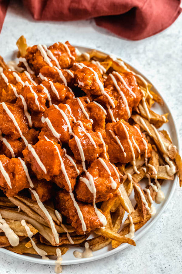 plate of buffalo chicken bites and fries drizzled with spicy aioli sauce