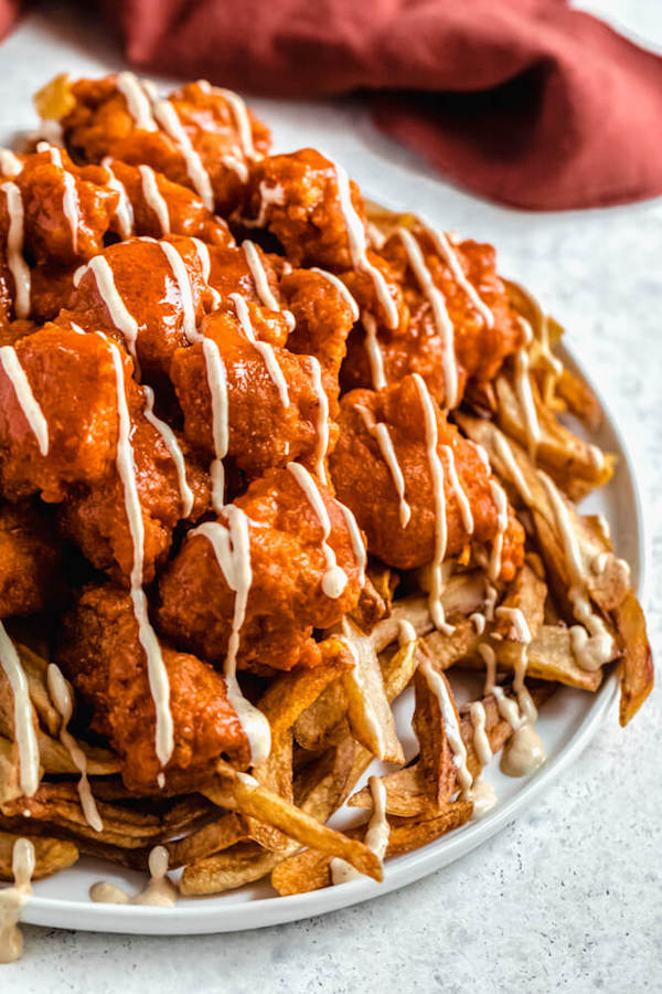 close up of a plate of fries with boneless buffalo chicken bites drizzled with spicy aioli