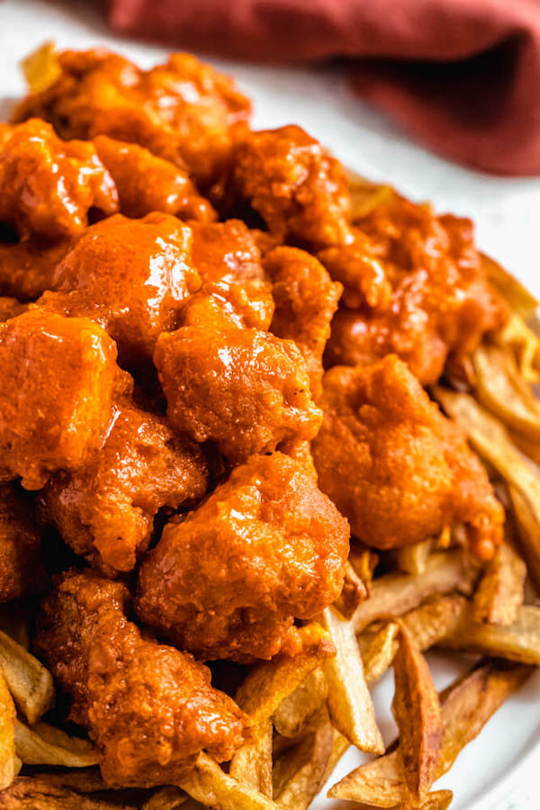 close up of chicken pieces coated in buffalo sauce piled on top of homemade fries