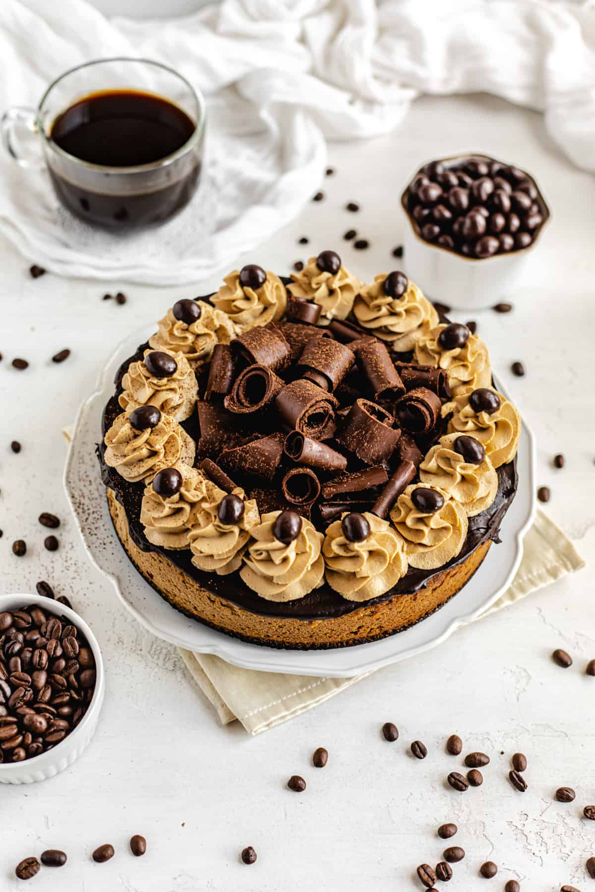 cheesecake on a white platter surrounded by coffee and coffee beans