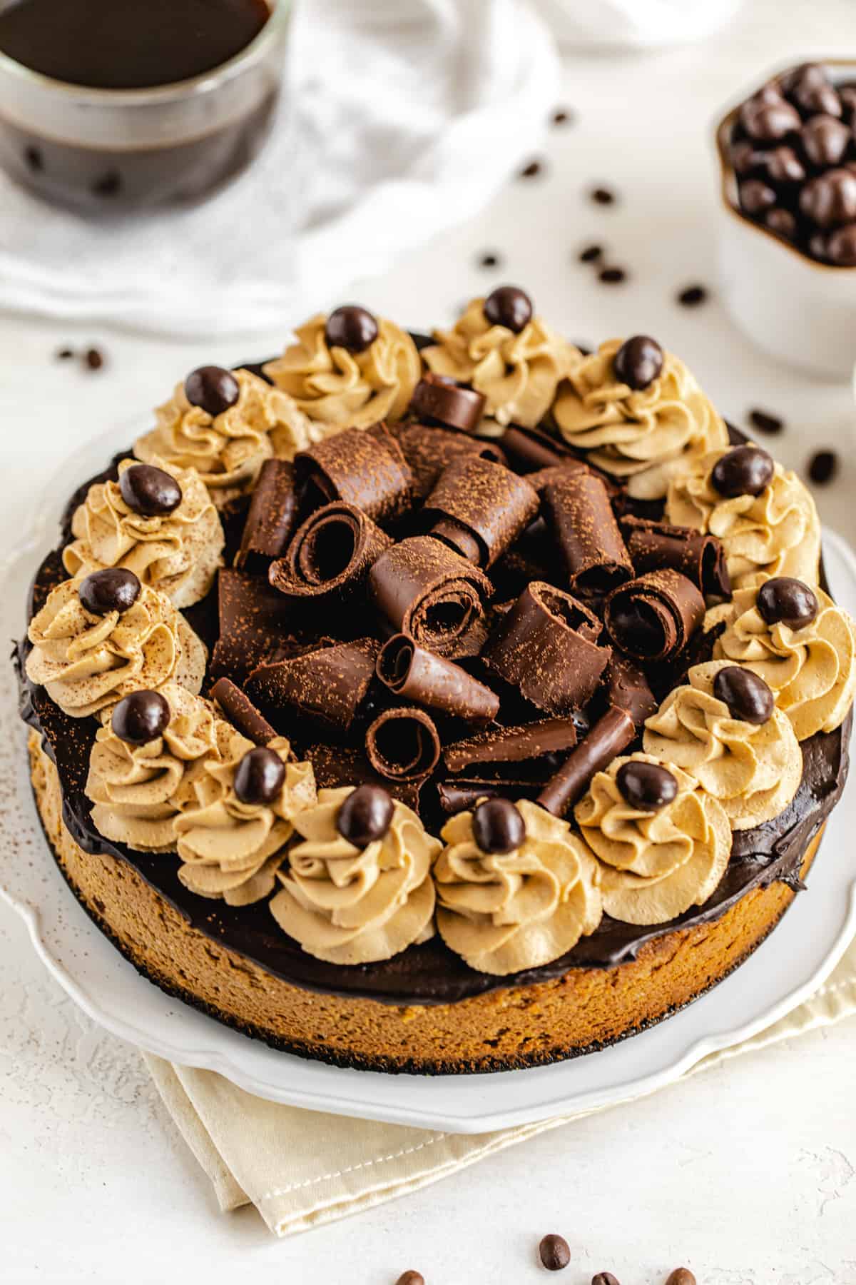 close up of cheesecake on a white platter with coffee in the back