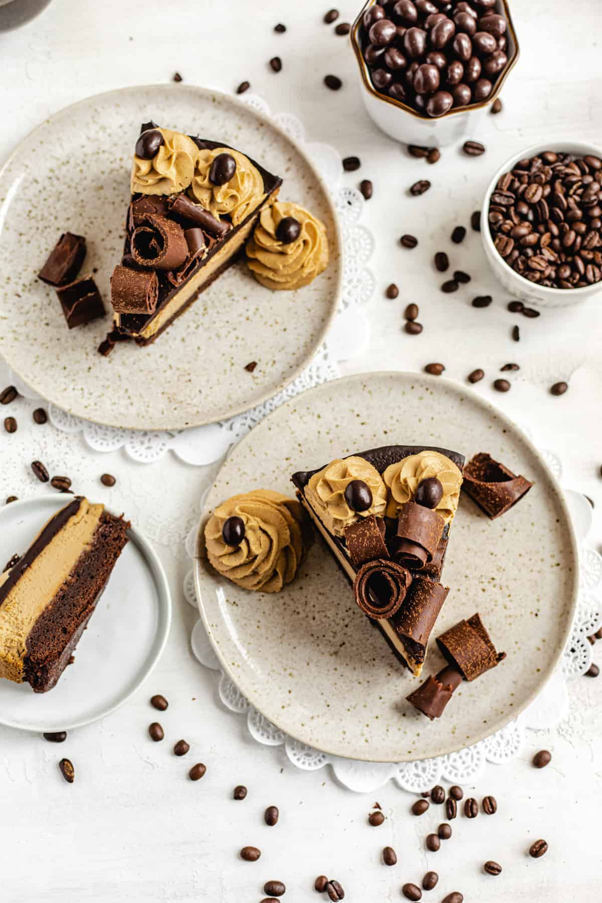 three slices of cheesecake on three plates with coffee beans around them