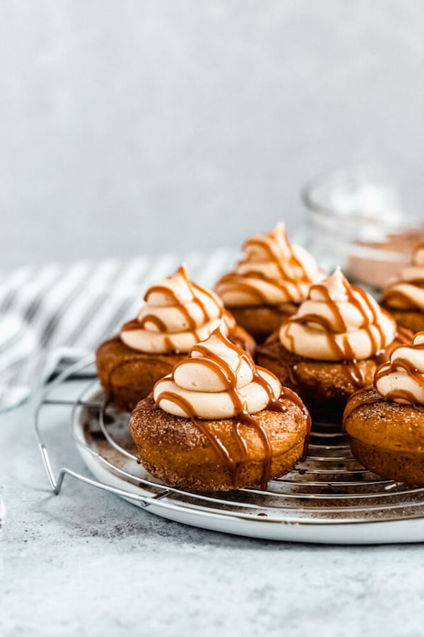 pumpkin donuts topped with salted caramel cream cheese frosting and salted caramel sauce drizzle on a round wire rack