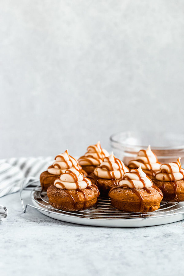 pumpkin donuts topped with salted caramel cream cheese frosting and salted caramel sauce drizzle on a round wire rack