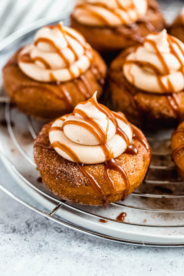 pumpkin donuts topped with salted caramel cream cheese frosting and salted caramel sauce drizzle on a round wire rack