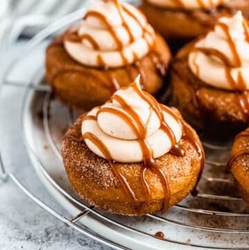 pumpkin donuts topped with salted caramel cream cheese frosting and salted caramel sauce drizzle on a round wire rack