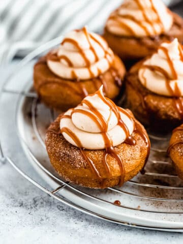 pumpkin donuts topped with salted caramel cream cheese frosting and salted caramel sauce drizzle on a round wire rack