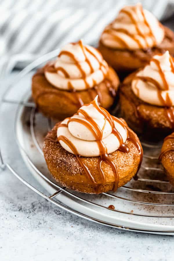 pumpkin donuts topped with salted caramel cream cheese frosting and salted caramel sauce drizzle on a round wire rack