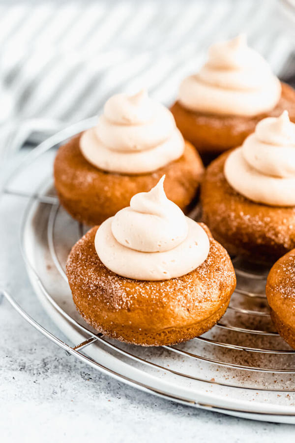 pumpkin donuts topped with salted caramel cream cheese frosting on a round wire rack