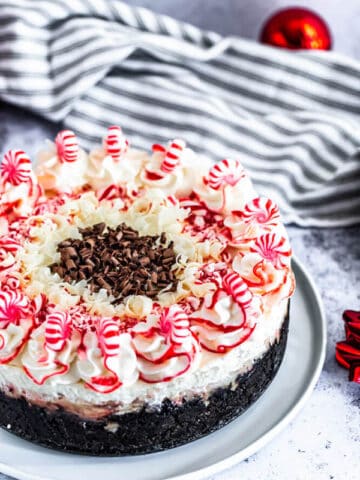 peppermint bark cheesecake on a white plate with striped dish towel in the back