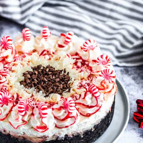 peppermint bark cheesecake on a white plate with striped dish towel in the back