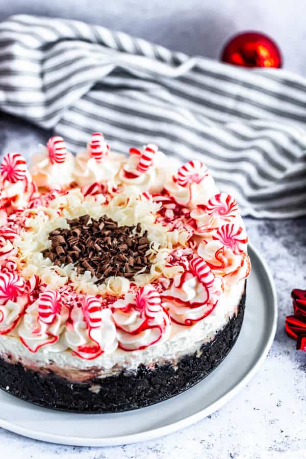 peppermint bark cheesecake on a white plate with striped dish towel in the back