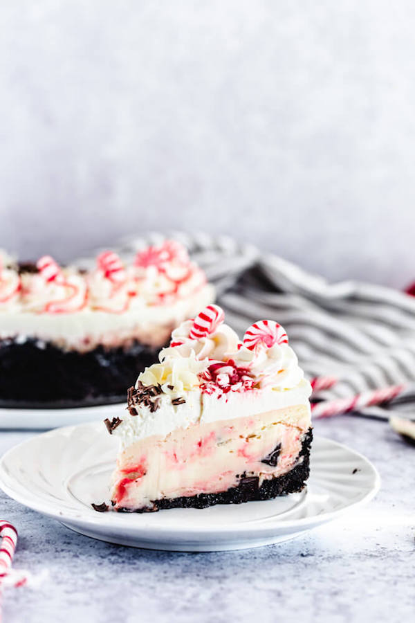 candy cane bark cheesecake slice on a plate with full cheesecake in background