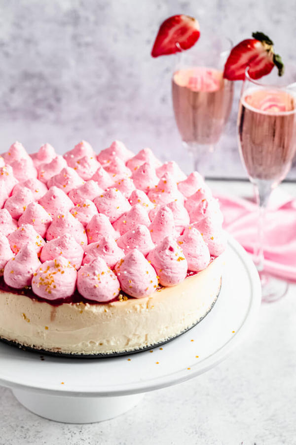 cheesecake topped with strawberry whipped cream on a cake stand