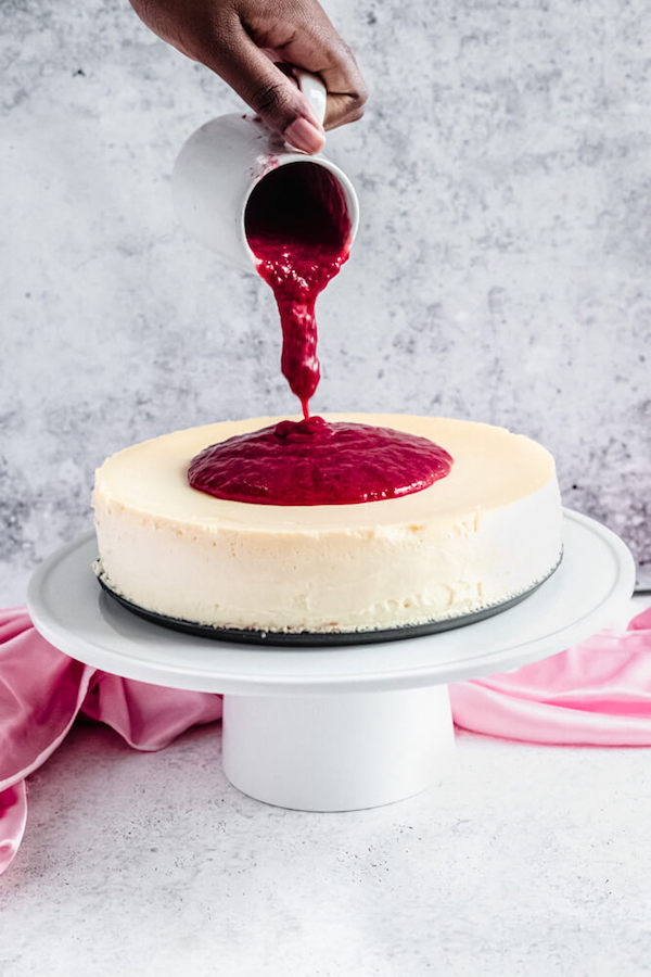 pouring strawberry sauce onto cheesecake