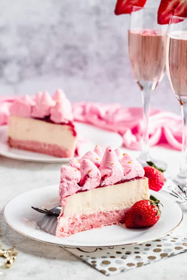 slice of champagne cheesecake on a white plate with a strawberry on the side