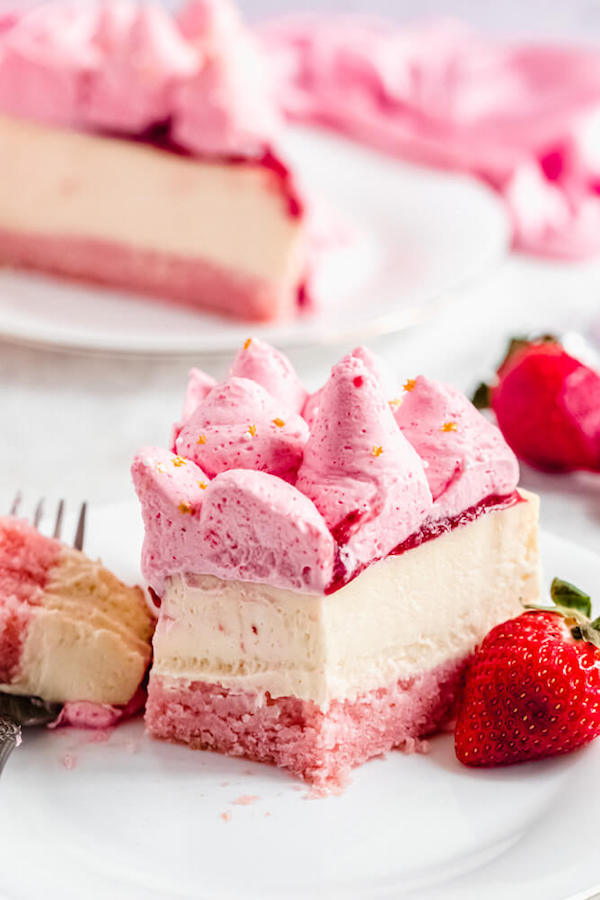 half a slice of champagne and strawberry cheesecake on a white plate with a strawberry beside it