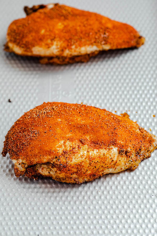 two seasoned chicken breasts on a sheet pan