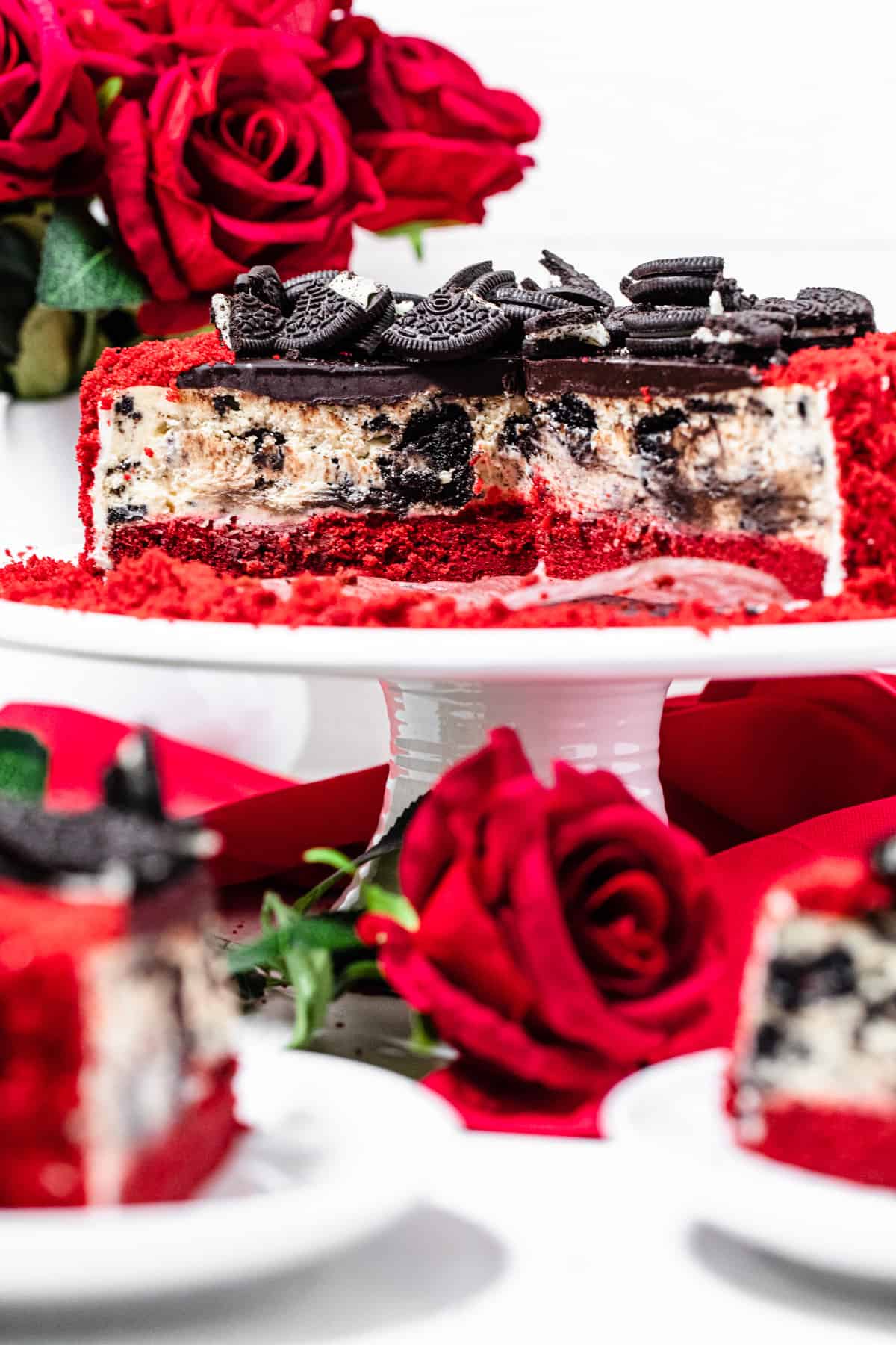 halved cheesecake on a white cake stand with roses and plates with cheesecake slices in front