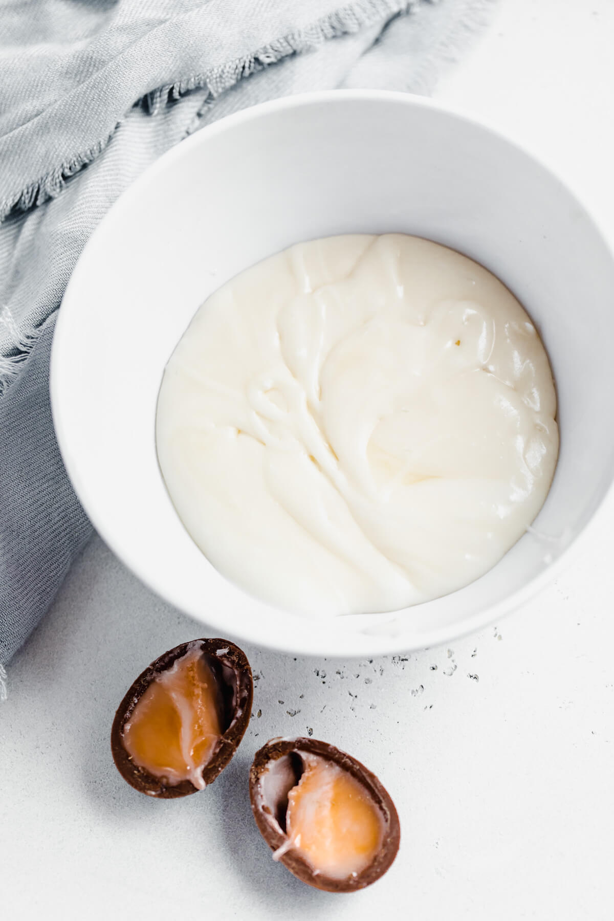 homemade creme egg filling in a white bowl with a halved creme egg beside it