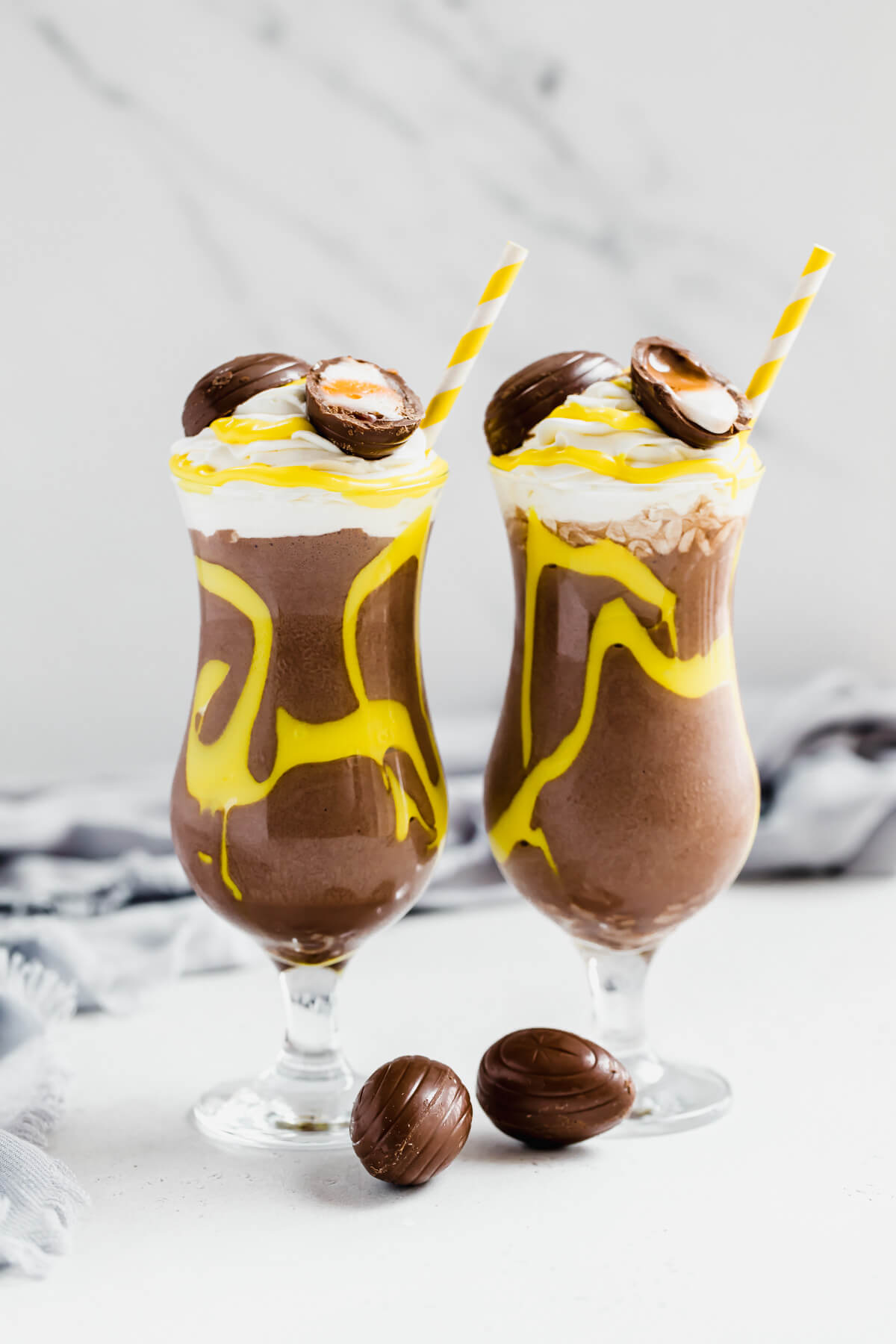 two glasses of chocolate milkshake decorated with yellow creme egg filling and topped with Cadbury creme eggs