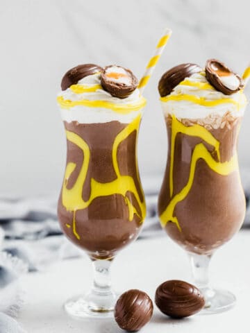 two glasses of milkshake topped with Cadbury creme eggs