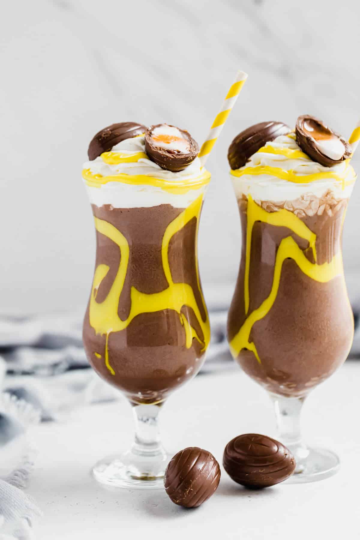 two glasses of chocolate milkshake with a homemade creme egg filling decoration and topping 