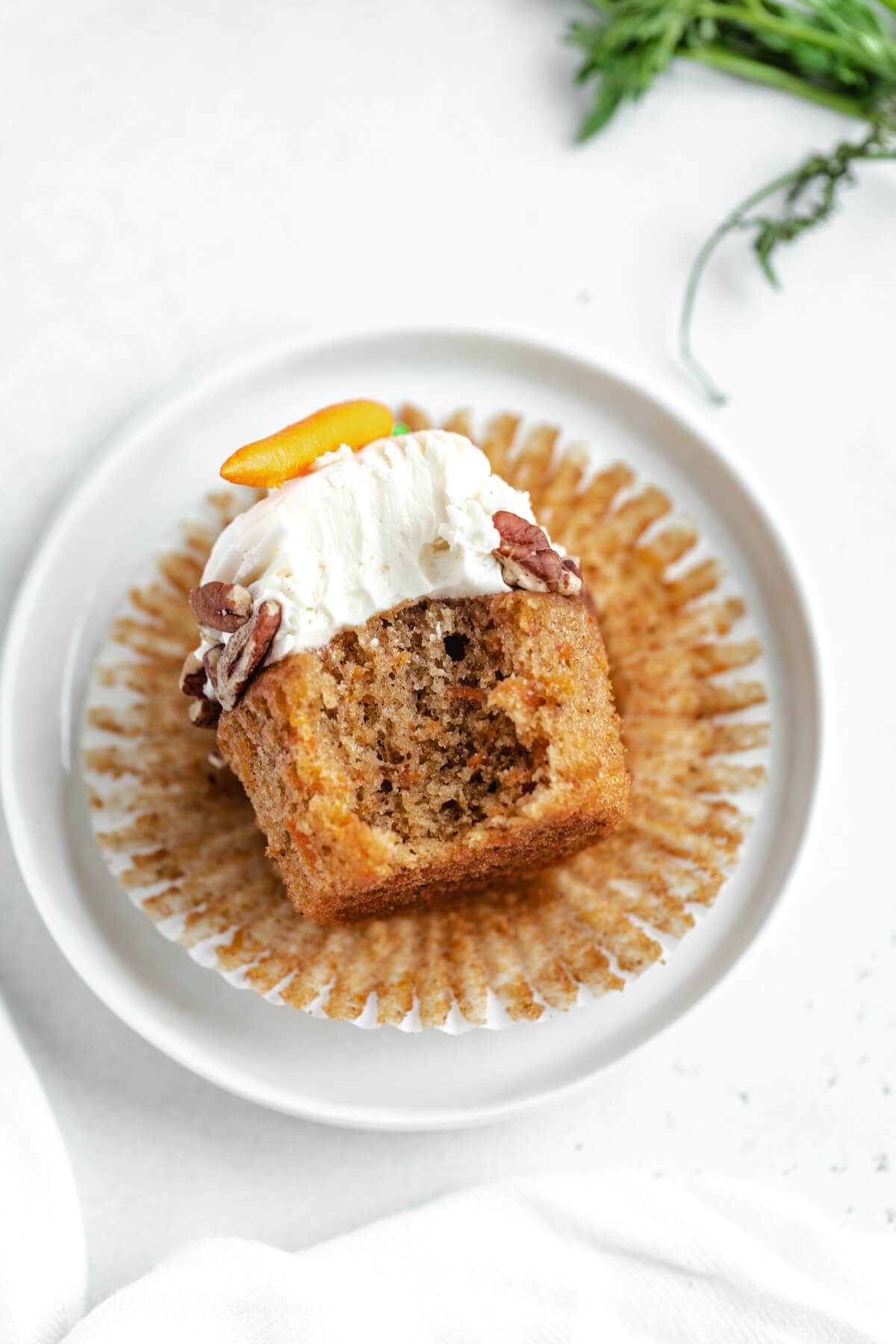 cupcake with a bite taken out of it laying down on its wrapper and a small white plate