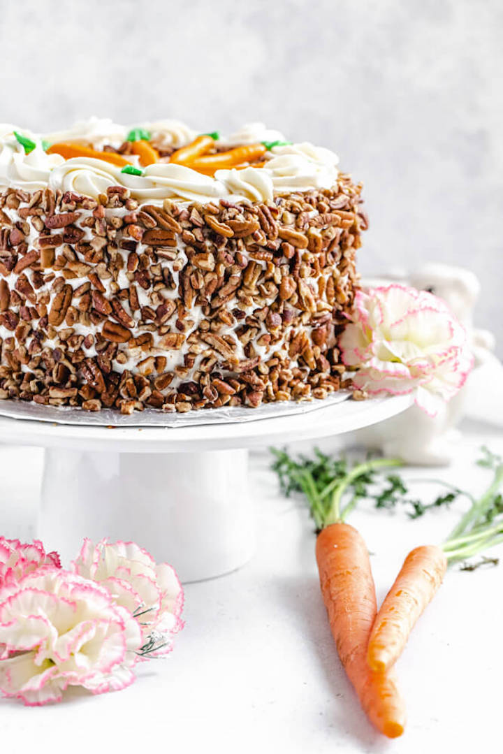 cake covered in pecans on a cake stand with flowers