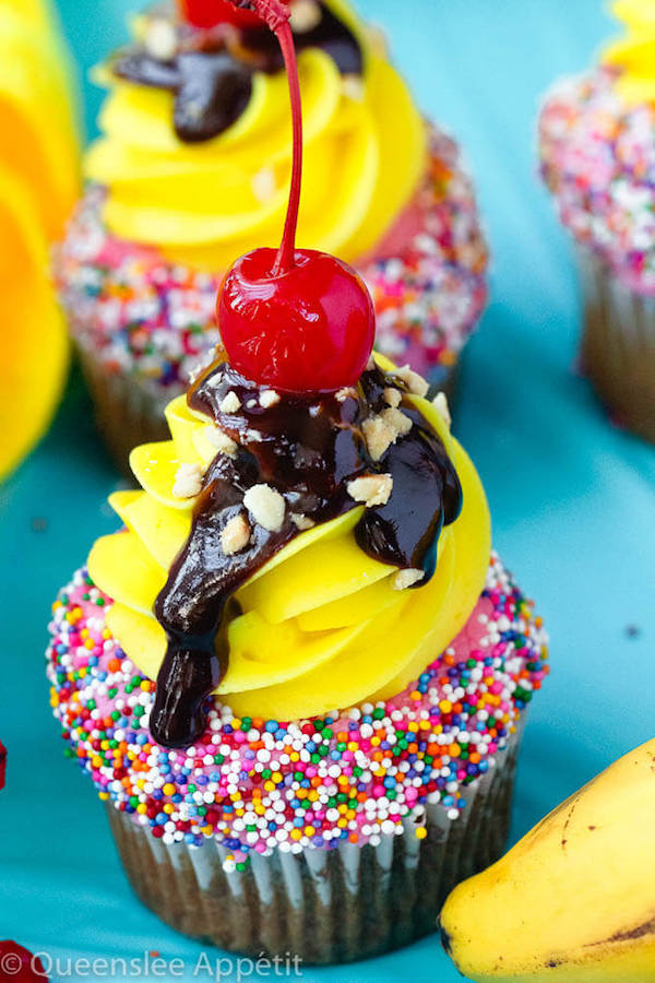 moist and delicious banana cupcake that’s been decorated with strawberry and vanilla buttercream, colourful sprinkles, chocolate sauce, chopped nuts and a bright red cherry on top