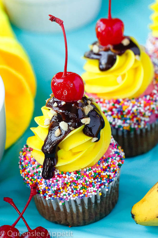 moist and delicious banana cupcake that’s been decorated with strawberry and vanilla buttercream, colourful sprinkles, chocolate sauce, chopped nuts and a bright red cherry on top