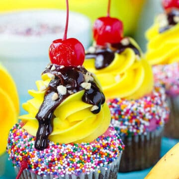moist and delicious banana cupcake that’s been decorated with strawberry and vanilla buttercream, colourful sprinkles, chocolate sauce, chopped nuts and a bright red cherry on top