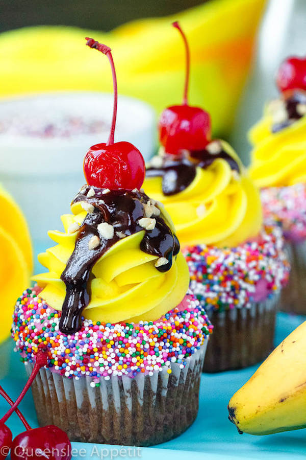 moist and delicious banana cupcake that’s been decorated with strawberry and vanilla buttercream, colourful sprinkles, chocolate sauce, chopped nuts and a bright red cherry on top