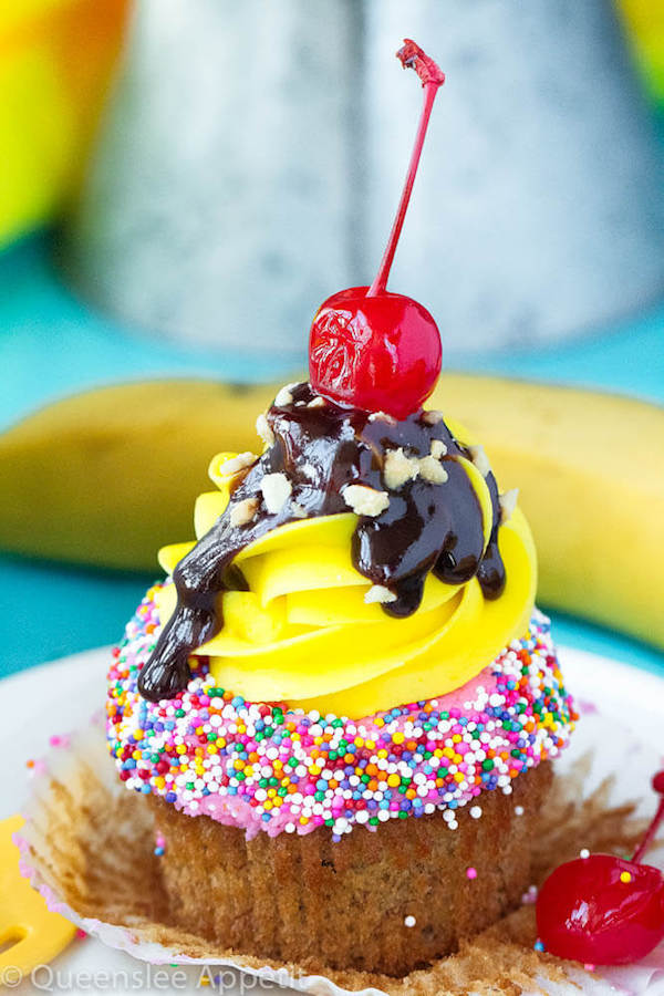 moist and delicious banana cupcake that’s been decorated with strawberry and vanilla buttercream, colourful sprinkles, chocolate sauce, chopped nuts and a bright red cherry on top