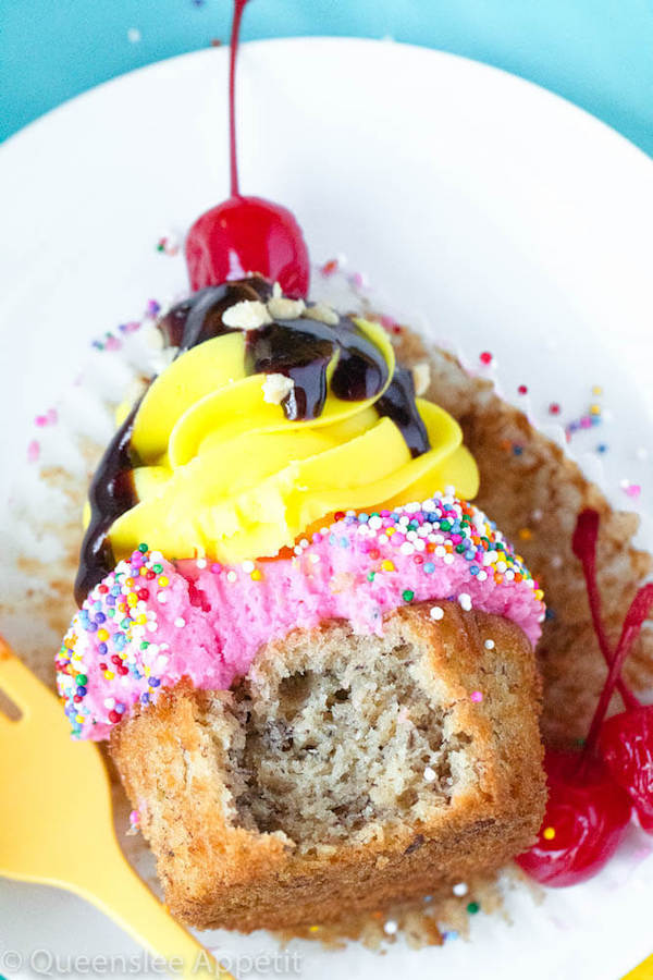 moist and delicious banana cupcake that’s been decorated with strawberry and vanilla buttercream, colourful sprinkles, chocolate sauce, chopped nuts and a bright red cherry on top