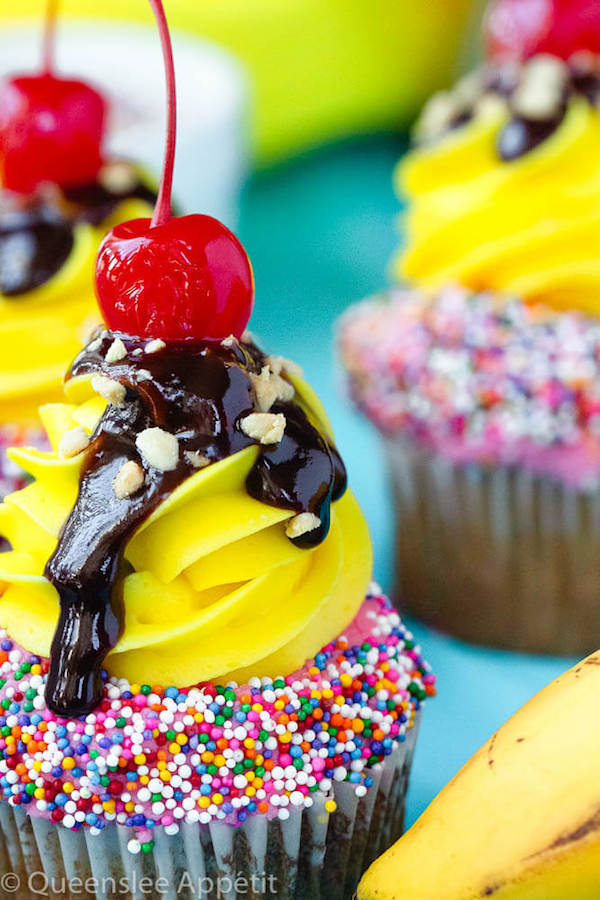 moist and delicious banana cupcake that’s been decorated with strawberry and vanilla buttercream, colourful sprinkles, chocolate sauce, chopped nuts and a bright red cherry on top