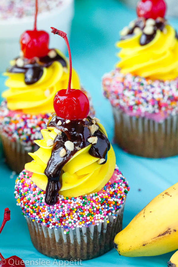 moist and delicious banana cupcake that’s been decorated with strawberry and vanilla buttercream, colourful sprinkles, chocolate sauce, chopped nuts and a bright red cherry on top