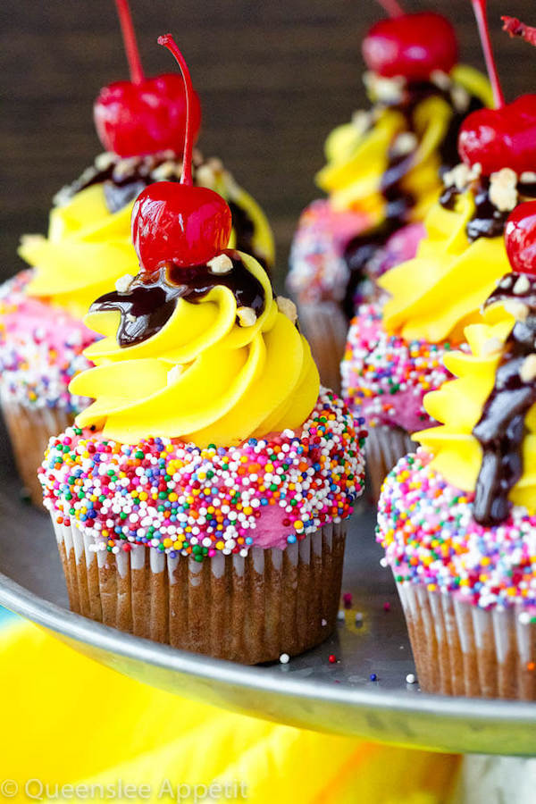 moist and delicious banana cupcake that’s been decorated with strawberry and vanilla buttercream, colourful sprinkles, chocolate sauce, chopped nuts and a bright red cherry on top