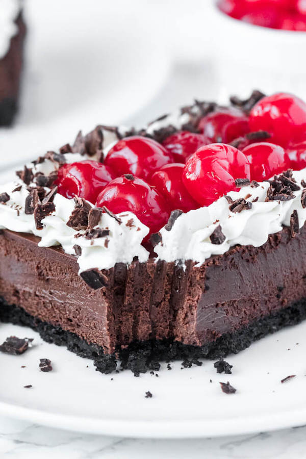 chocolate cheesecake bars with whipped cream, cherries and chocolate shavings