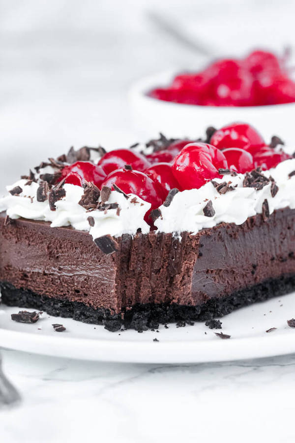 chocolate cheesecake bars with whipped cream, cherries and chocolate shavings