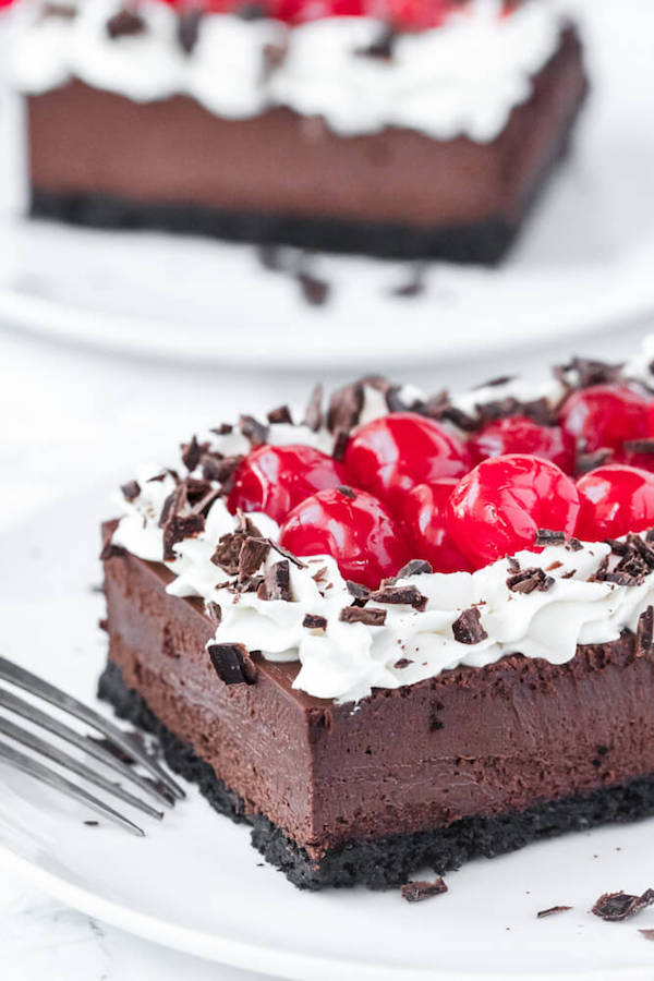 chocolate cheesecake bars with whipped cream, cherries and chocolate shavings