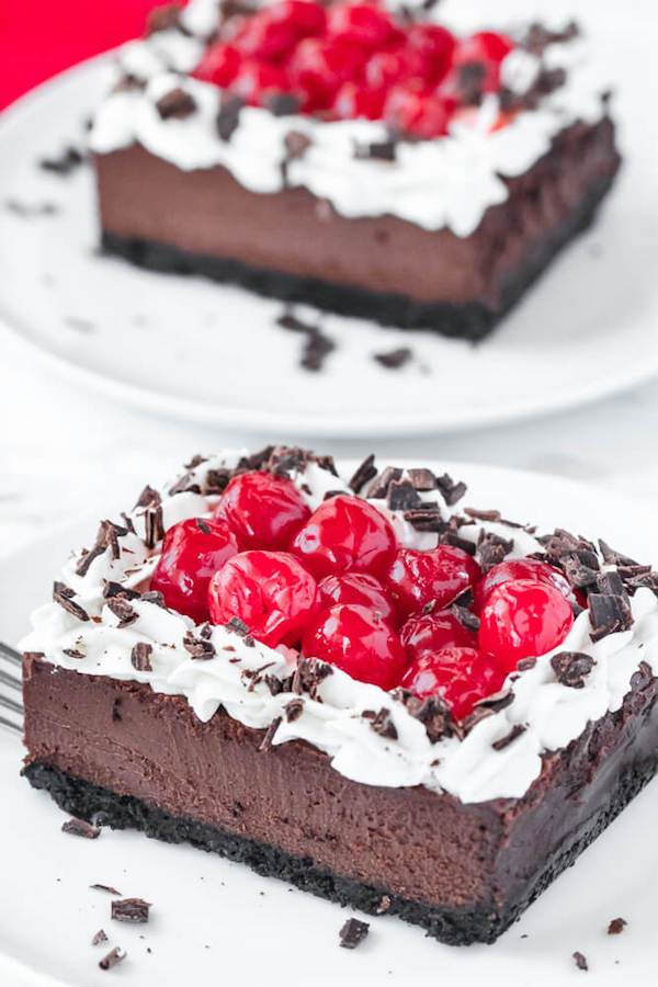 chocolate cheesecake bars with whipped cream, cherries and chocolate shavings