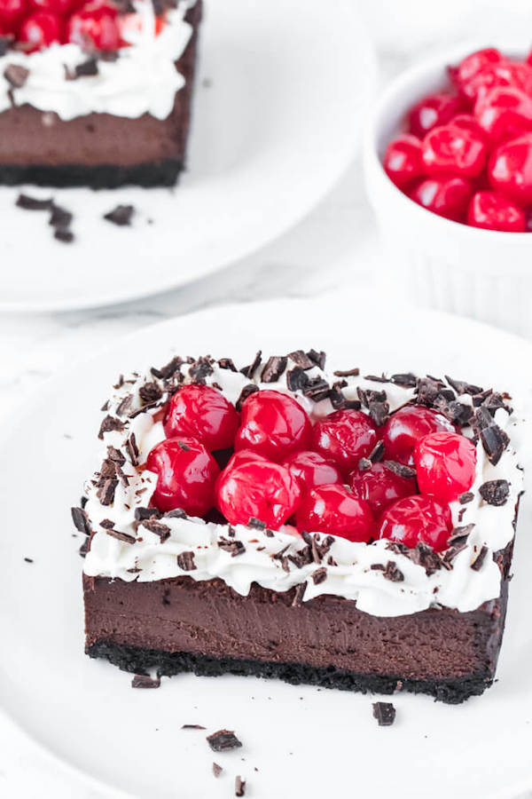 chocolate cheesecake bars with whipped cream, cherries and chocolate shavings