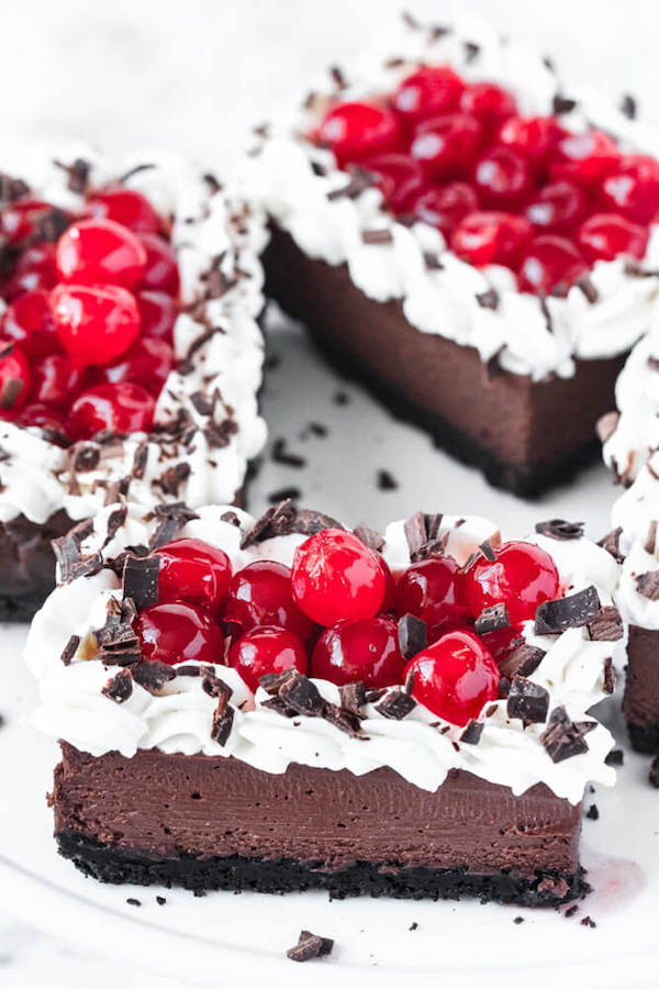chocolate cheesecake bars with whipped cream, cherries and chocolate shavings