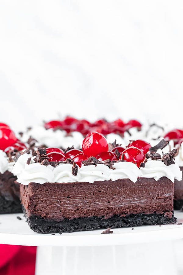 chocolate cheesecake bars with whipped cream, cherries and chocolate shavings