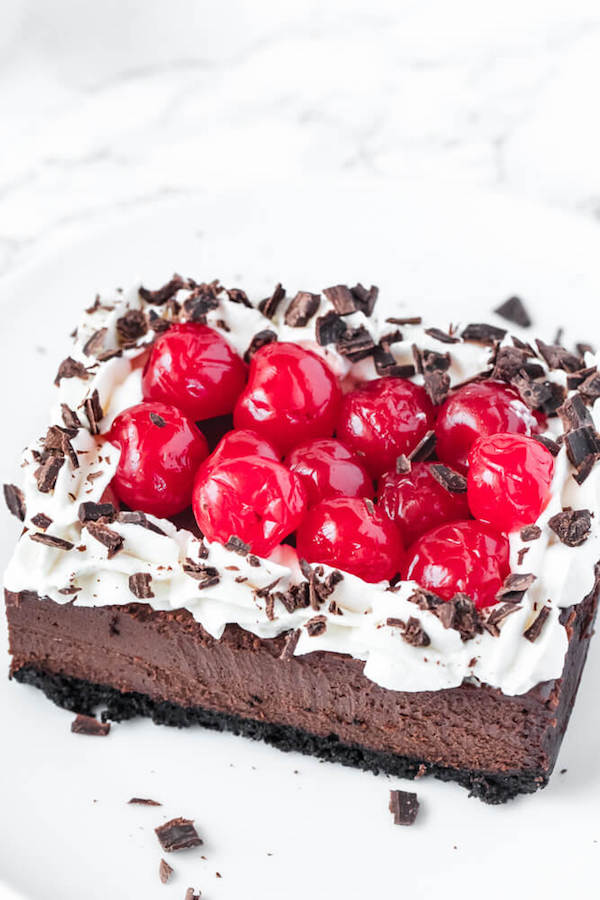 chocolate cheesecake bars with whipped cream, cherries and chocolate shavings