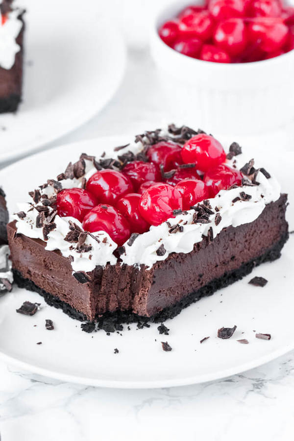 chocolate cheesecake bars with whipped cream, cherries and chocolate shavings