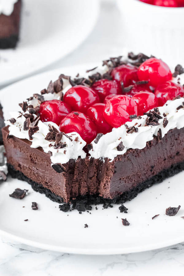 chocolate cheesecake bars with whipped cream, cherries and chocolate shavings