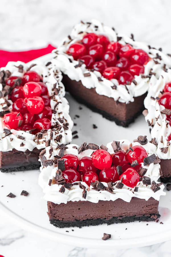 chocolate cheesecake bars with whipped cream, cherries and chocolate shavings