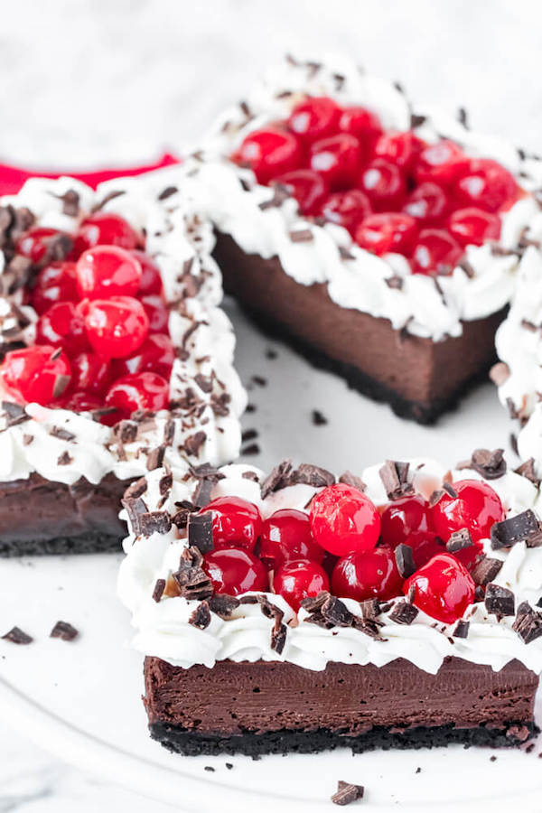 chocolate cheesecake bars with whipped cream, cherries and chocolate shavings